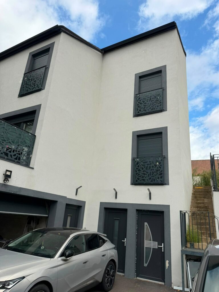 Façade d’un bâtiment d’habitation aux volets gris, avec des voitures au premier plan.