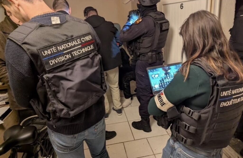 Coco : 819 gendarmes mobilisés, l’UNCyber détaille les coulisses de l’enquête Enquêteurs portant des gilets Unité nationale cyber dans une pièce, dont une enquêtrice tenant un ordinateur portable.