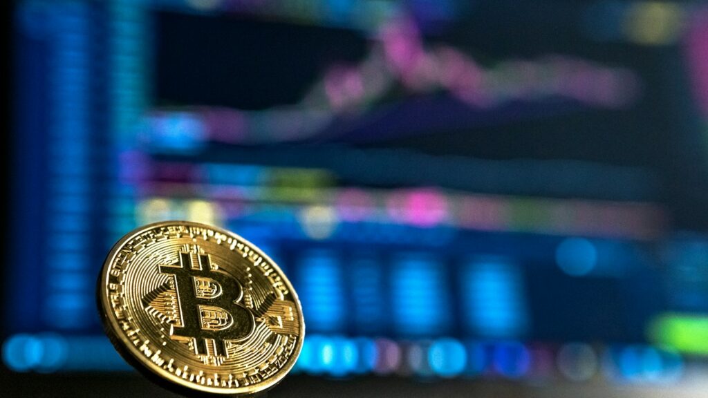 Crypto-actifs : cinq interpellations après une séquestration en Haute-Savoie Jeton doré portant le symbole Bitcoin devant un écran de graphiques flou.