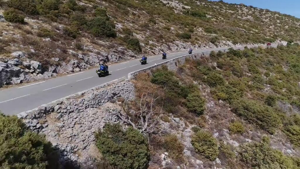 Quatre motocyclistes en uniforme bleu sur une route de montagne, vus du ciel.