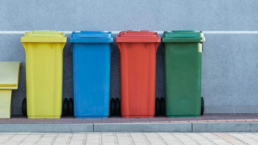 Pézenas : collectes maintenues et déchèteries fermées les 1er et 11 novembre Quatre bacs de déchets colorés alignés contre un mur, photographie d’illustration.