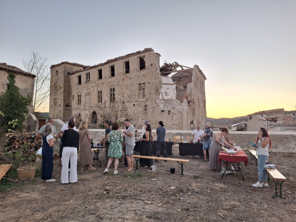 Des habitants réunis autour de tables pour une fête des voisins devant le château endommagé de Pomas.