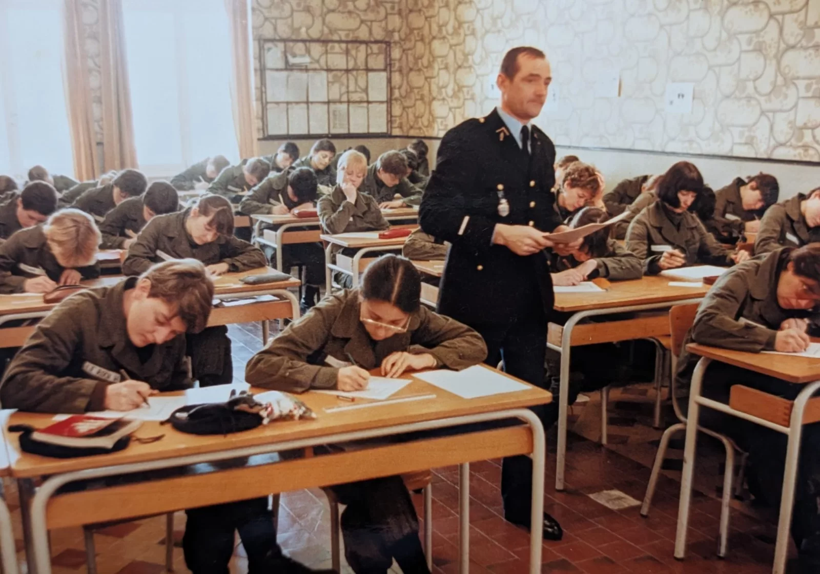 Des élèves en uniforme travaillent à leur table dans une salle de cours, en présence d’un instructeur.