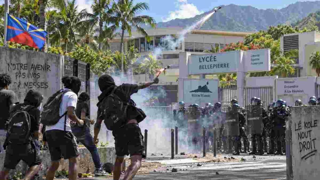 La Réunion : deux gendarmes blessés, un véhicule caillassé, 18 interpellations Illustration générée par IA montrant des affrontements devant un lycée à La Réunion, avec des gendarmes et des projectiles